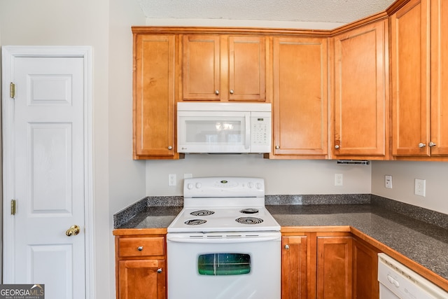 kitchen with white appliances, brown cabinetry, and dark countertops