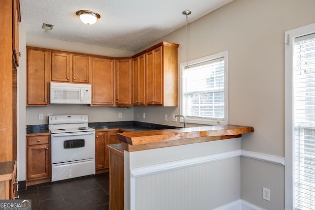 kitchen with white appliances, plenty of natural light, dark countertops, brown cabinets, and pendant lighting