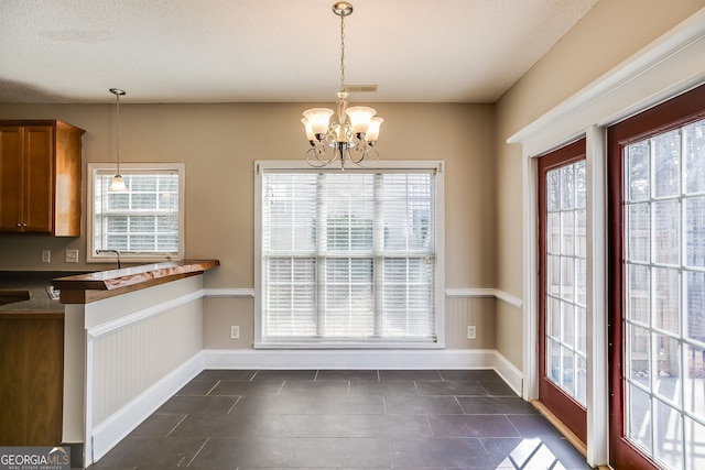 unfurnished dining area with a wealth of natural light, a textured ceiling, and an inviting chandelier