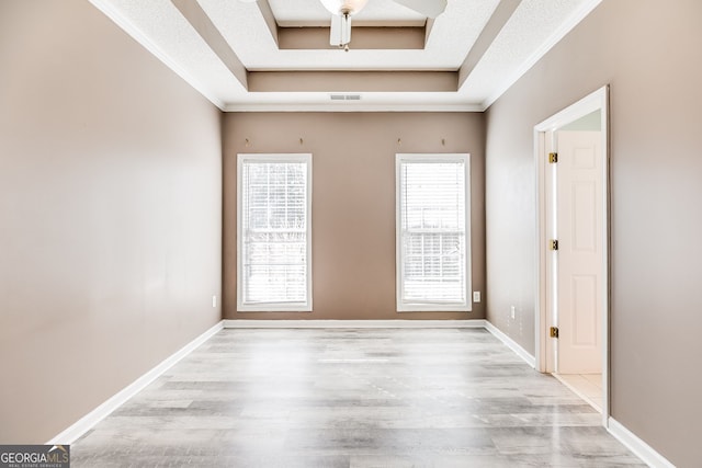 empty room featuring light wood-style flooring, visible vents, a tray ceiling, and baseboards