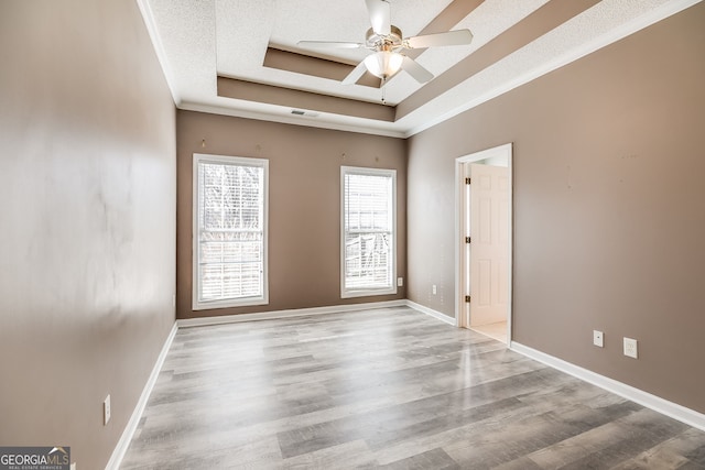 spare room with a tray ceiling, visible vents, ceiling fan, light wood-type flooring, and baseboards