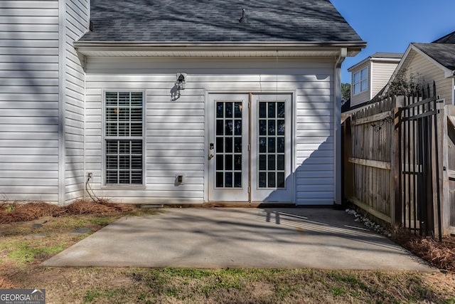 property entrance with a shingled roof, a patio area, and fence