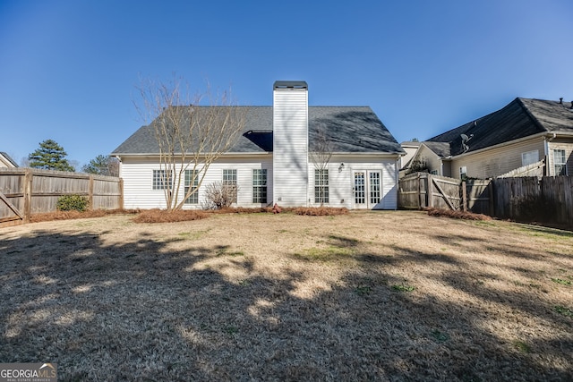 rear view of property featuring a yard, a chimney, and a fenced backyard