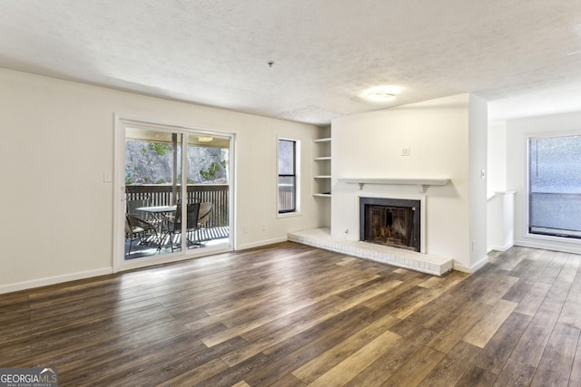 unfurnished living room with a wealth of natural light, dark wood-style flooring, a textured ceiling, and baseboards