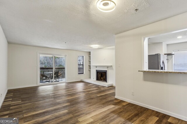 2701 Cumberland Ct SE, Smyrna, GA 30080 - unfurnished living room featuring a textured ceiling, baseboards, built in features, a brick fireplace, and dark wood-style floors