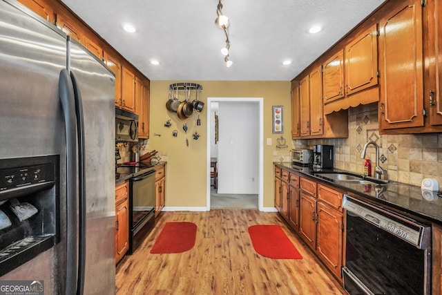 kitchen with brown cabinetry, light wood-style flooring, a sink, black appliances, and backsplash