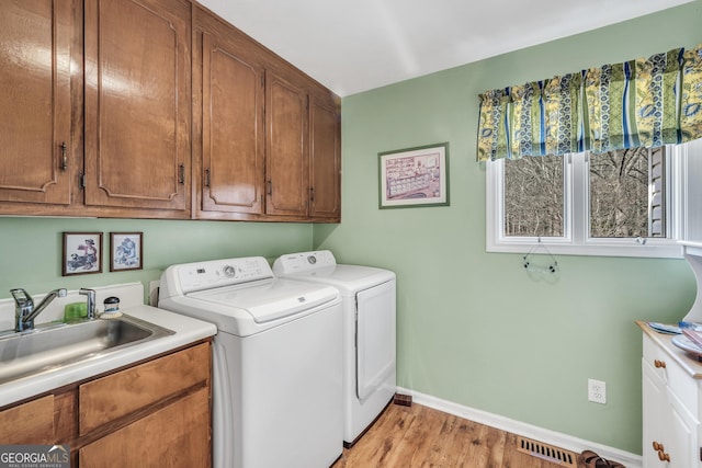 clothes washing area with washing machine and dryer, light wood-style flooring, a sink, baseboards, and cabinet space