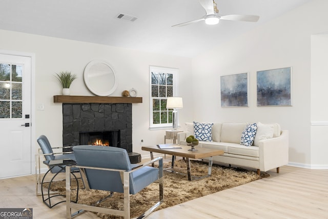 living area featuring lofted ceiling, ceiling fan, light wood-style flooring, a fireplace, and visible vents