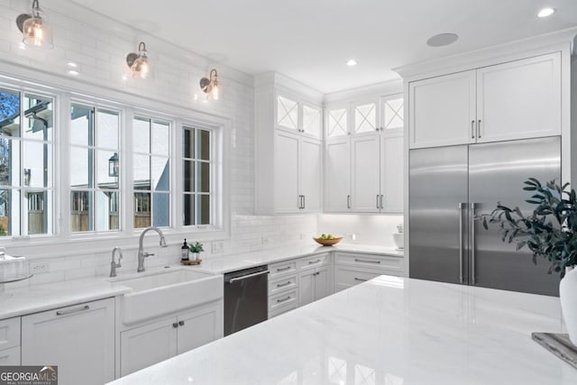 kitchen with tasteful backsplash, appliances with stainless steel finishes, white cabinetry, a sink, and light stone countertops