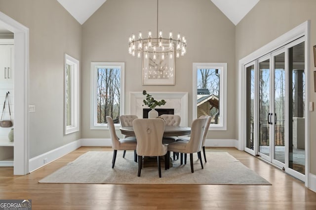 dining space featuring baseboards, high vaulted ceiling, light wood-type flooring, and an inviting chandelier