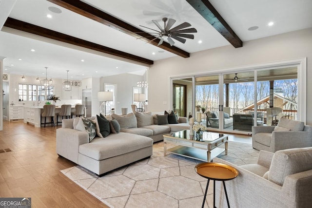 living room with ceiling fan with notable chandelier, beamed ceiling, light wood-style flooring, and recessed lighting