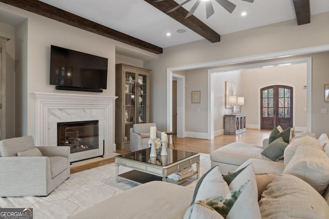 living room with baseboards, beamed ceiling, french doors, light wood-type flooring, and a high end fireplace