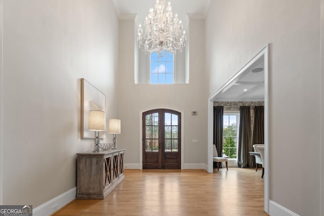 foyer featuring a chandelier, baseboards, french doors, ornamental molding, and light wood finished floors