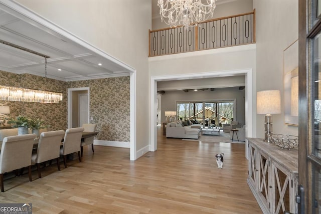 foyer featuring baseboards, wallpapered walls, wood finished floors, and an inviting chandelier