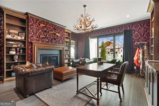 office featuring a notable chandelier, wood finished floors, wallpapered walls, a glass covered fireplace, and crown molding