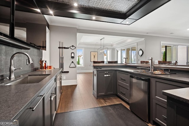 kitchen featuring decorative light fixtures, dark countertops, a raised ceiling, stainless steel dishwasher, and a sink