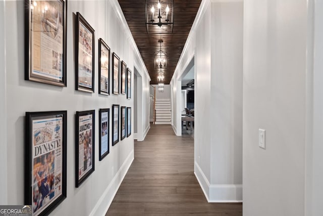 hall with dark wood-style flooring, wood ceiling, baseboards, stairs, and an inviting chandelier