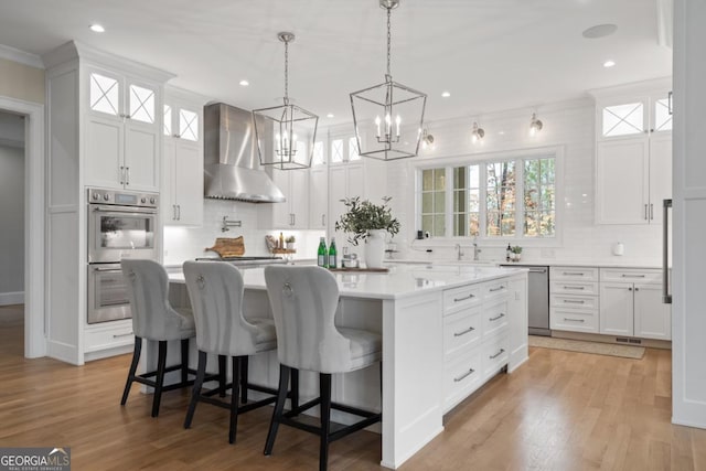 kitchen with stainless steel appliances, a kitchen island, white cabinetry, light countertops, and wall chimney exhaust hood