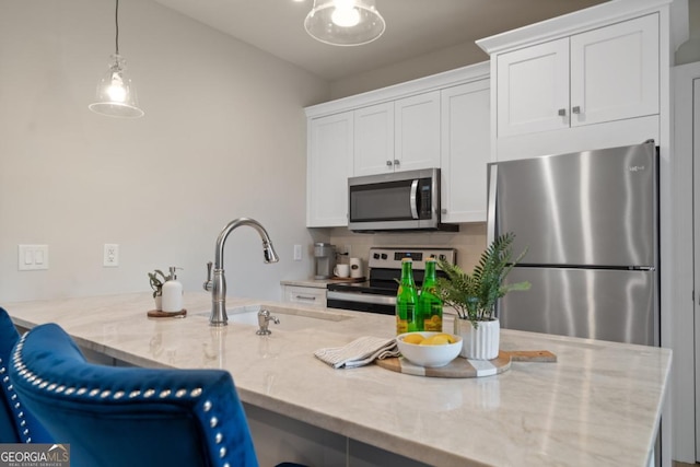 kitchen with white cabinets, appliances with stainless steel finishes, light stone counters, pendant lighting, and a sink