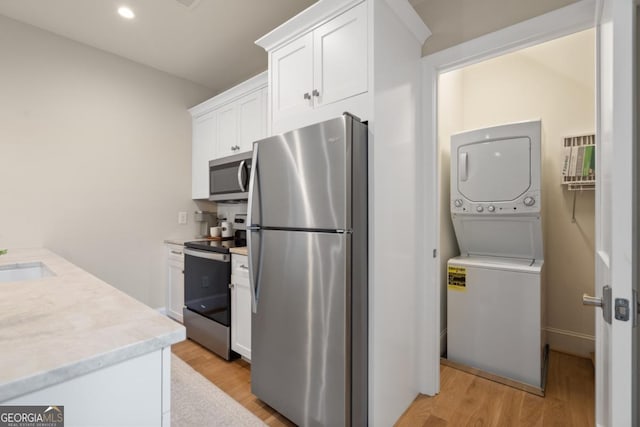 kitchen featuring stacked washer and dryer, appliances with stainless steel finishes, light countertops, light wood-style floors, and white cabinetry