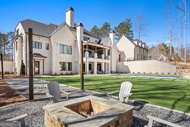 back of property featuring stucco siding, a lawn, an outdoor fire pit, a balcony, and a residential view