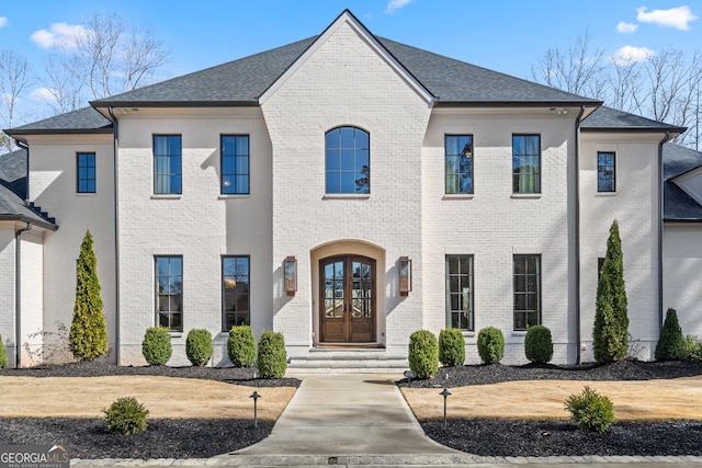 french provincial home featuring french doors, brick siding, and roof with shingles