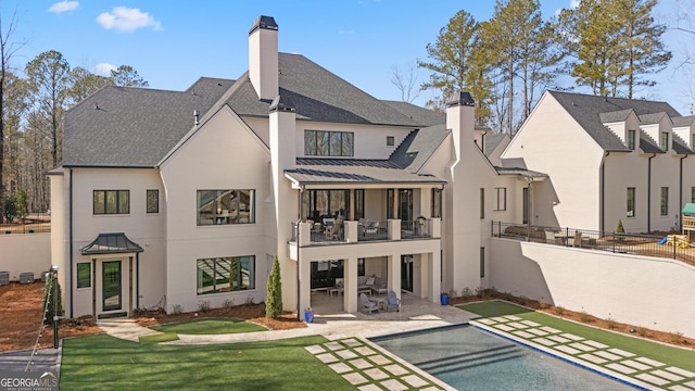 rear view of property featuring a standing seam roof, a chimney, a fenced backyard, and an outdoor pool