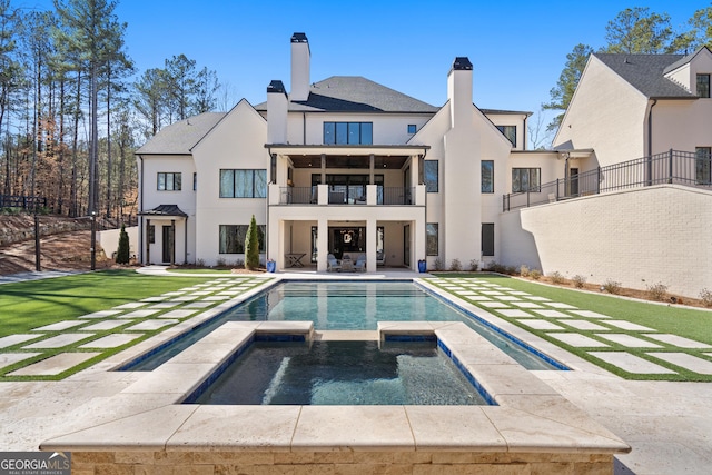 back of property with a lawn, a balcony, a patio area, a pool with connected hot tub, and stucco siding