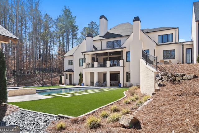 rear view of house featuring brick siding, a chimney, stucco siding, a balcony, and an outdoor pool