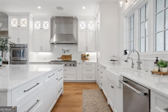 kitchen featuring appliances with stainless steel finishes, white cabinetry, glass insert cabinets, and wall chimney exhaust hood