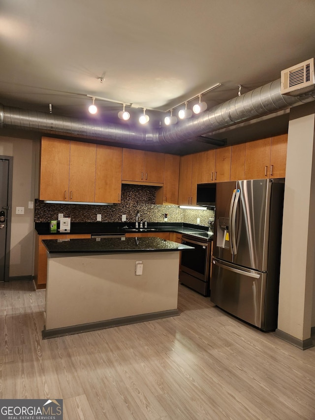 kitchen featuring light wood finished floors, stainless steel appliances, dark countertops, tasteful backsplash, and visible vents