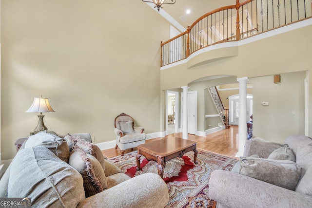 living room featuring decorative columns, arched walkways, baseboards, a high ceiling, and light wood-type flooring