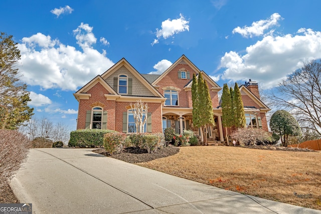 craftsman-style house featuring a chimney, a front lawn, and brick siding