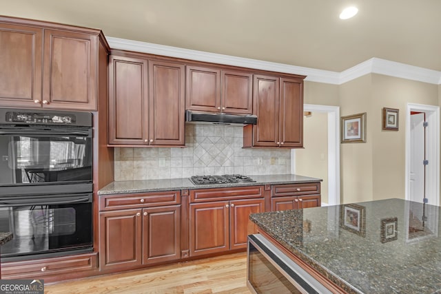 kitchen featuring dobule oven black, stainless steel gas stovetop, ornamental molding, dark stone countertops, and under cabinet range hood