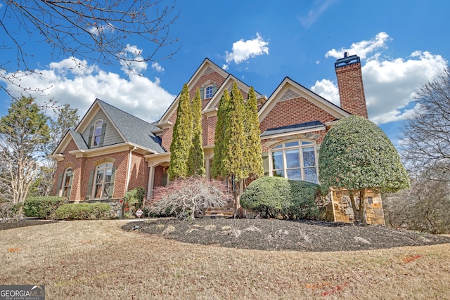 view of front of house featuring a front yard, a chimney, and brick siding