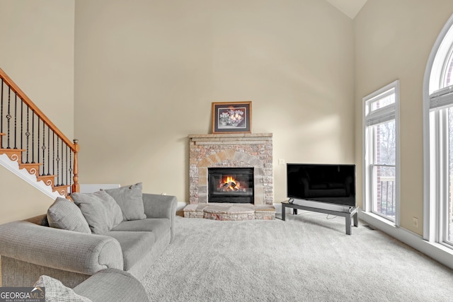 carpeted living area with stairs, a stone fireplace, and a high ceiling