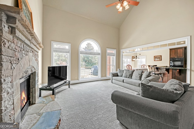 living room with light carpet, high vaulted ceiling, a stone fireplace, and a ceiling fan