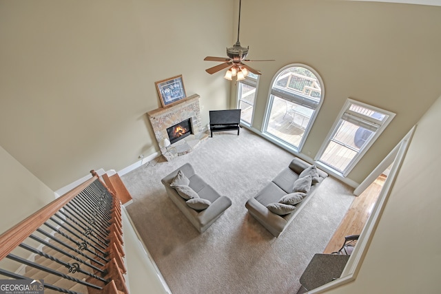 living area with a stone fireplace, carpet, a towering ceiling, and baseboards