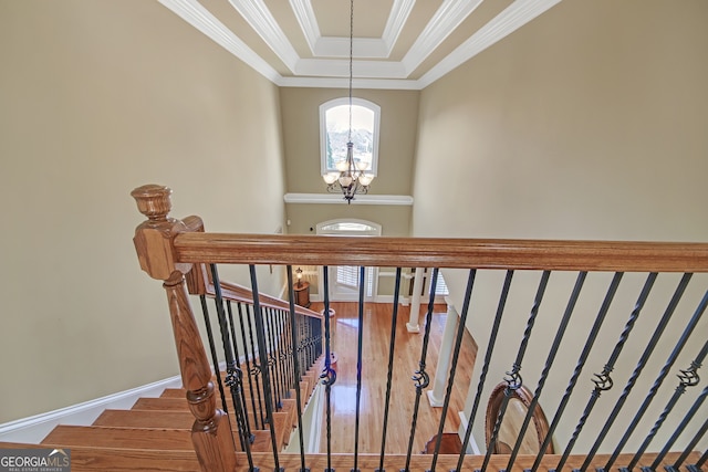 stairway with a raised ceiling, an inviting chandelier, ornamental molding, wood finished floors, and baseboards