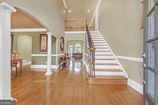 entrance foyer featuring arched walkways, baseboards, stairway, light wood finished floors, and decorative columns