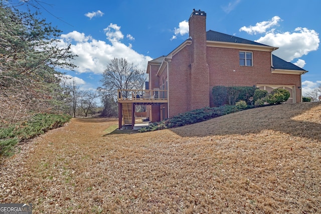 view of side of home featuring a chimney, stairway, a deck, a yard, and brick siding