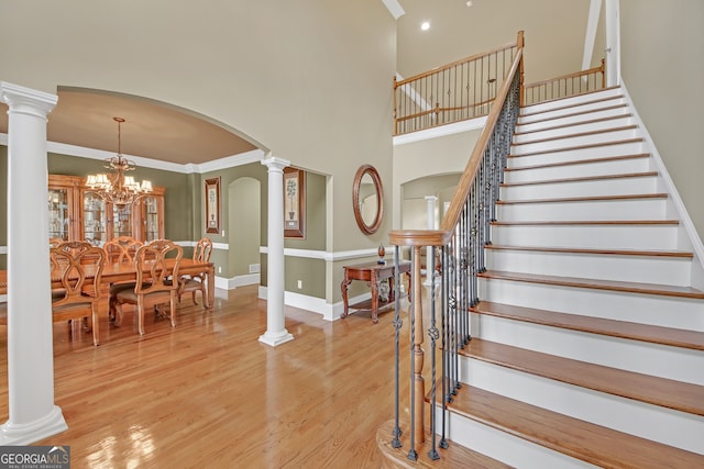 stairs with arched walkways, wood finished floors, a towering ceiling, decorative columns, and an inviting chandelier