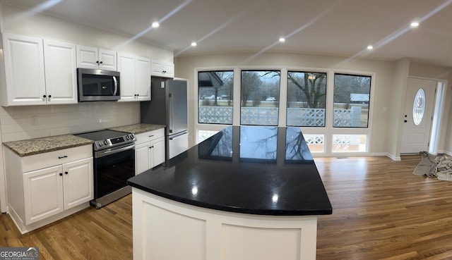 kitchen featuring wood finished floors, decorative backsplash, appliances with stainless steel finishes, white cabinetry, and a center island