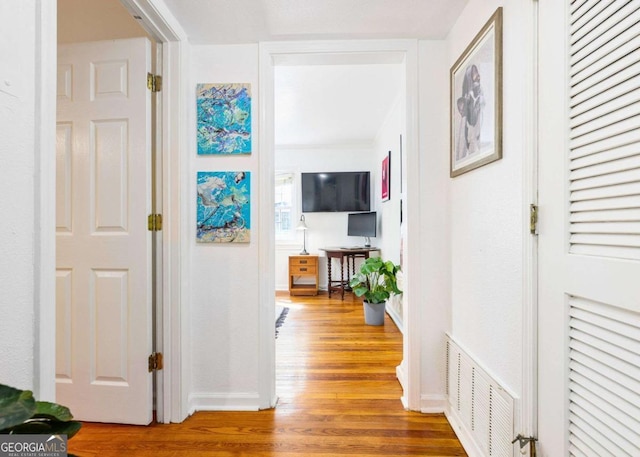 hallway with wood finished floors, visible vents, and baseboards