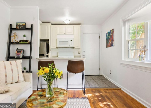 kitchen featuring white microwave, a breakfast bar area, wood finished floors, ornamental molding, and freestanding refrigerator