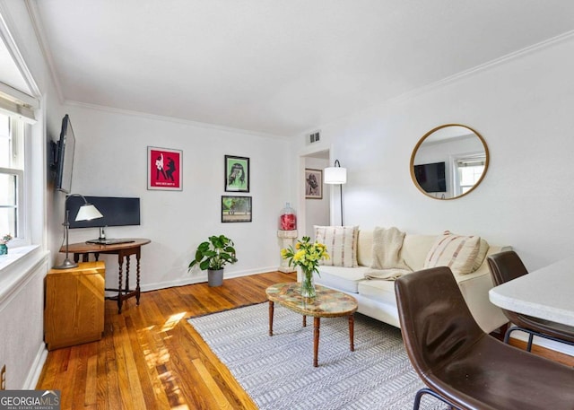 living area with baseboards, wood finished floors, visible vents, and crown molding