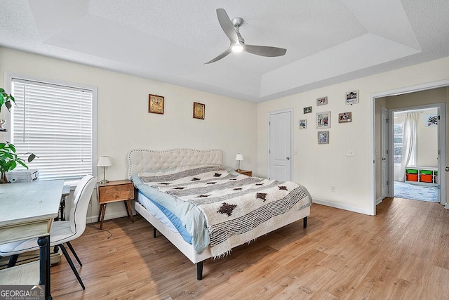 bedroom featuring light wood-style floors, a raised ceiling, and baseboards