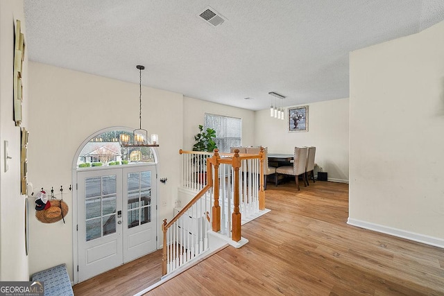 corridor with light wood-style flooring, visible vents, a notable chandelier, and an upstairs landing