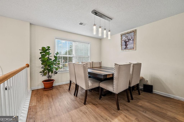 dining area with a textured ceiling, wood finished floors, visible vents, and baseboards