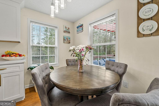 dining area featuring light wood-type flooring, a healthy amount of sunlight, a textured ceiling, and an inviting chandelier